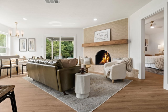 living room featuring a brick fireplace, plenty of natural light, ceiling fan with notable chandelier, and light hardwood / wood-style flooring