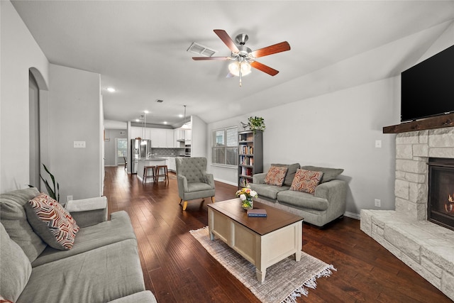 living room with vaulted ceiling, a stone fireplace, ceiling fan, and dark wood-type flooring