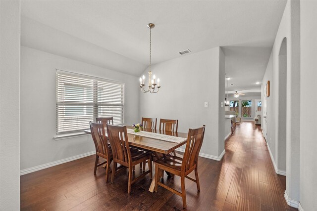 dining space featuring ceiling fan with notable chandelier, dark hardwood / wood-style floors, and vaulted ceiling