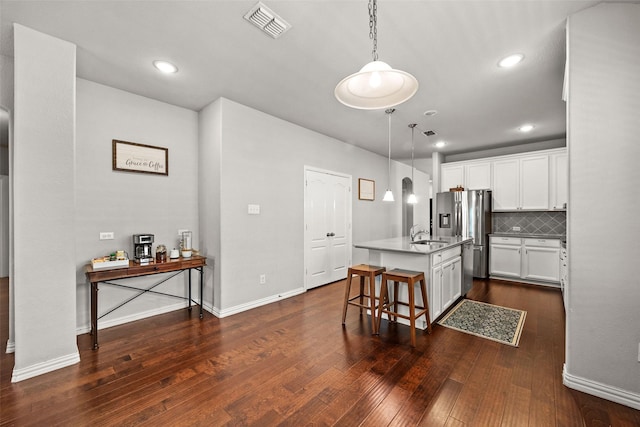 kitchen with white cabinetry, an island with sink, pendant lighting, a breakfast bar area, and decorative backsplash