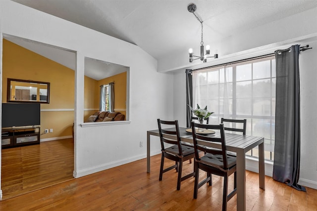 dining space with lofted ceiling, a notable chandelier, wood-type flooring, and plenty of natural light