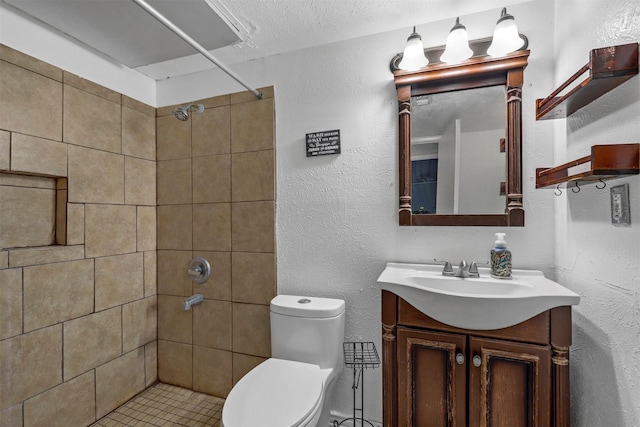 bathroom with a textured ceiling, tiled shower, vanity, and toilet