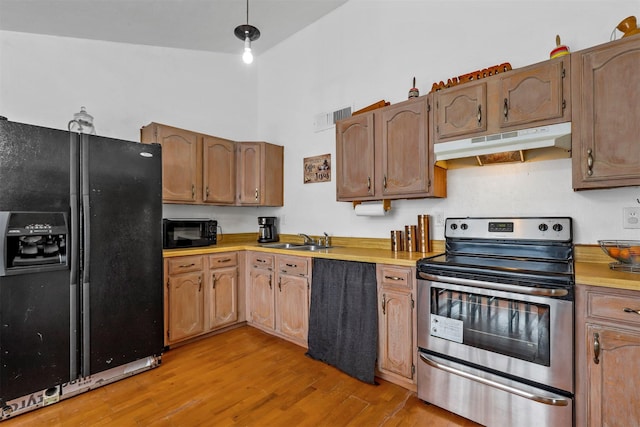 kitchen featuring a high ceiling, light wood-type flooring, black appliances, and sink