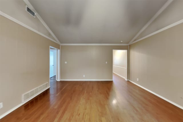 empty room featuring wood-type flooring, ornamental molding, and vaulted ceiling