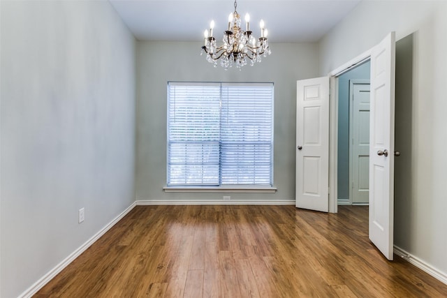 empty room with a chandelier and dark wood-type flooring