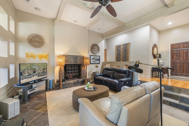 living room with beamed ceiling, a towering ceiling, ceiling fan, and a tiled fireplace