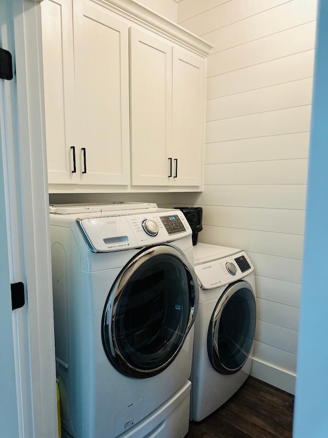 laundry room with cabinets, dark hardwood / wood-style floors, washer and clothes dryer, and wood walls