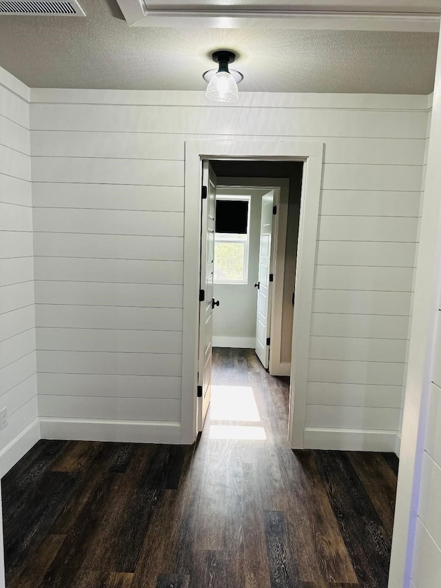 hallway featuring dark hardwood / wood-style floors, wooden walls, and a textured ceiling