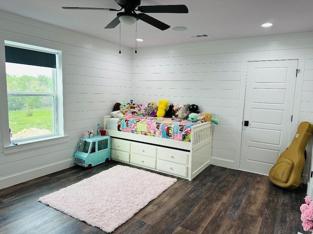 bedroom with dark hardwood / wood-style floors, ceiling fan, and wood walls