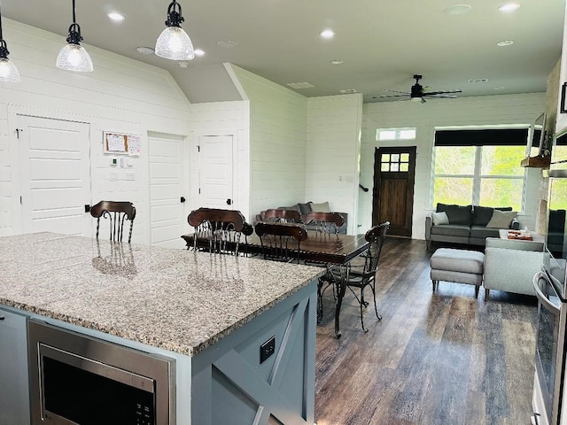 kitchen with a kitchen island, appliances with stainless steel finishes, hanging light fixtures, light stone counters, and dark wood-type flooring