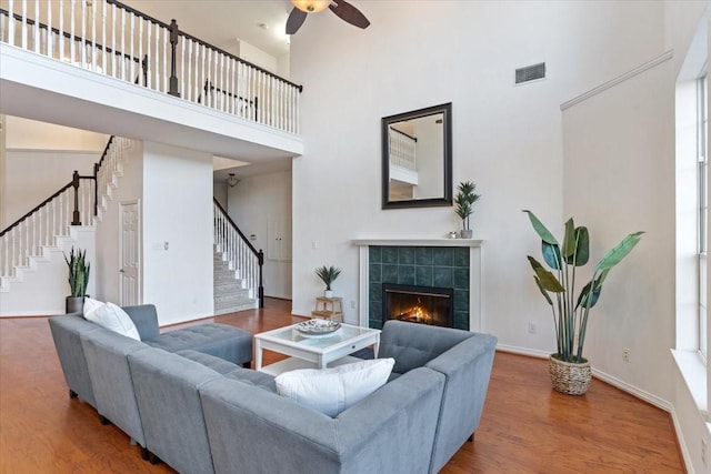 living area with a fireplace, visible vents, stairway, a high ceiling, and wood finished floors