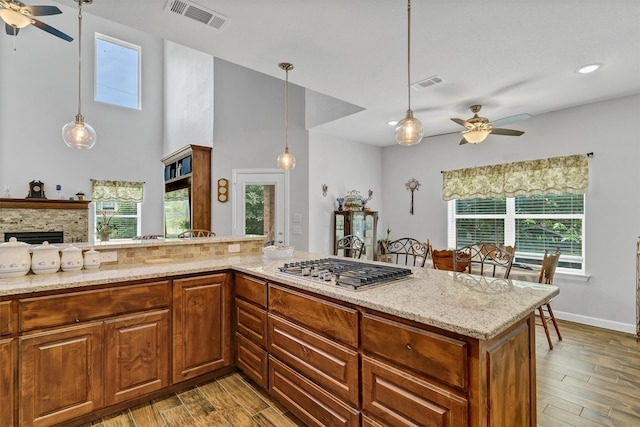 kitchen with ceiling fan, pendant lighting, a stone fireplace, light hardwood / wood-style floors, and light stone counters