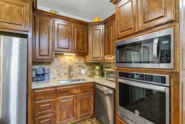 kitchen with sink, appliances with stainless steel finishes, wood-type flooring, light stone countertops, and tasteful backsplash