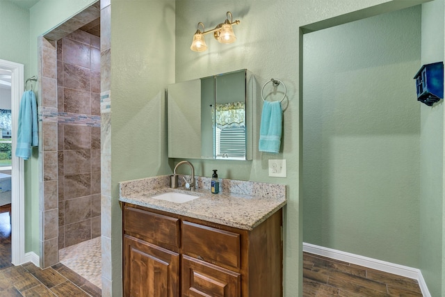 bathroom with tiled shower, hardwood / wood-style floors, and vanity