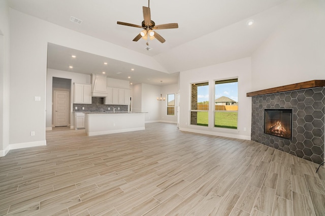 unfurnished living room with a tile fireplace, light wood-type flooring, ceiling fan, and lofted ceiling