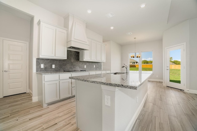 kitchen with premium range hood, a center island with sink, sink, light wood-type flooring, and white cabinetry