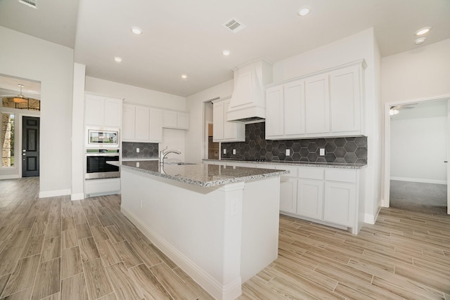 kitchen featuring stainless steel appliances, a kitchen island with sink, ceiling fan, light hardwood / wood-style floors, and white cabinetry