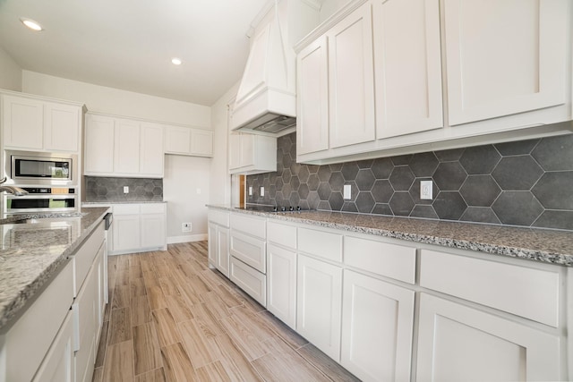 kitchen with white cabinetry, backsplash, appliances with stainless steel finishes, and light hardwood / wood-style flooring