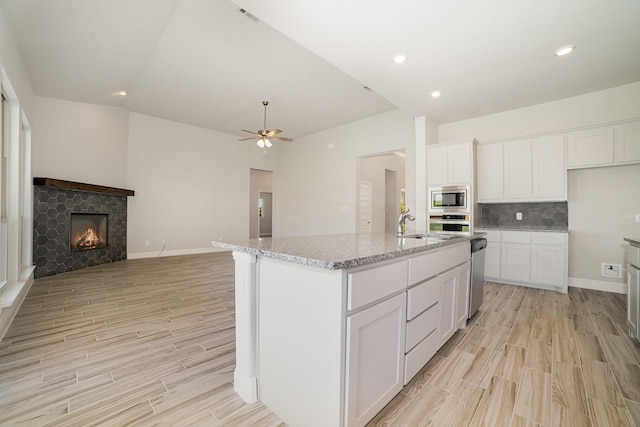 kitchen featuring light stone counters, stainless steel appliances, a center island with sink, a fireplace, and white cabinetry