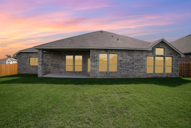 back house at dusk featuring a patio area and a yard