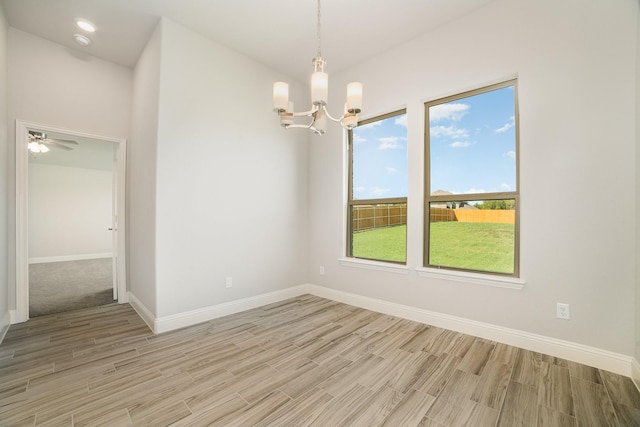 spare room with ceiling fan with notable chandelier and light wood-type flooring