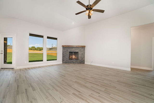 unfurnished living room with ceiling fan, lofted ceiling, a tiled fireplace, and light hardwood / wood-style flooring