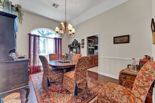 dining room featuring dark wood-type flooring, vaulted ceiling, and an inviting chandelier