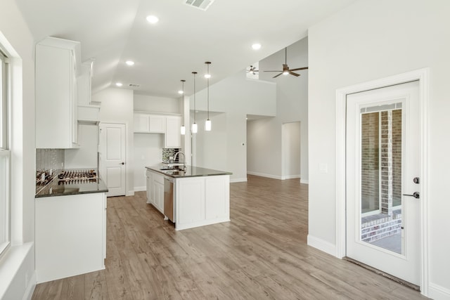 kitchen with light hardwood / wood-style floors, tasteful backsplash, white cabinetry, and a kitchen island with sink