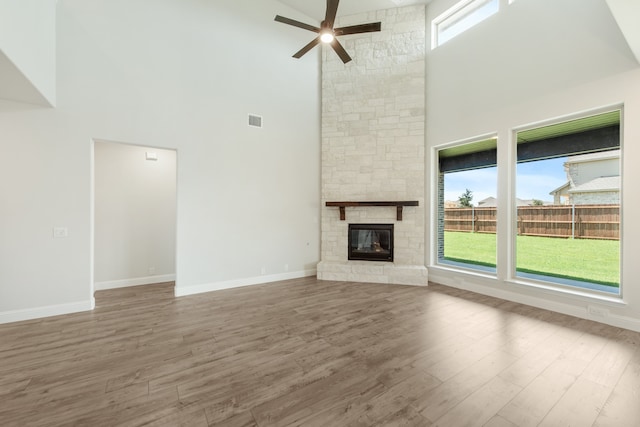 unfurnished living room with a high ceiling, hardwood / wood-style floors, ceiling fan, and a fireplace