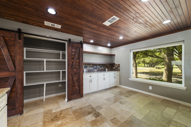 interior space featuring light stone countertops, tasteful backsplash, a barn door, wooden ceiling, and white cabinetry