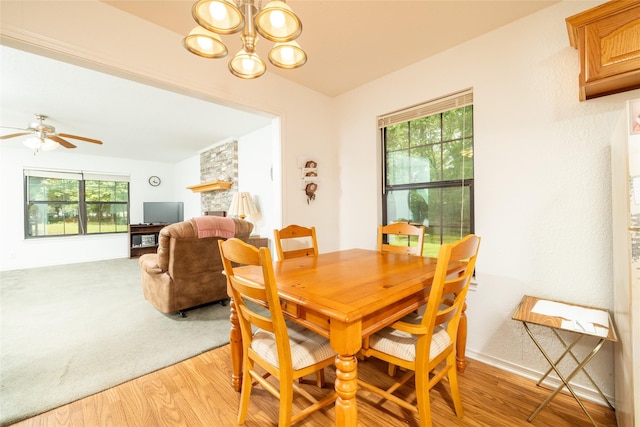 dining area featuring a stone fireplace, a healthy amount of sunlight, light hardwood / wood-style floors, and ceiling fan with notable chandelier