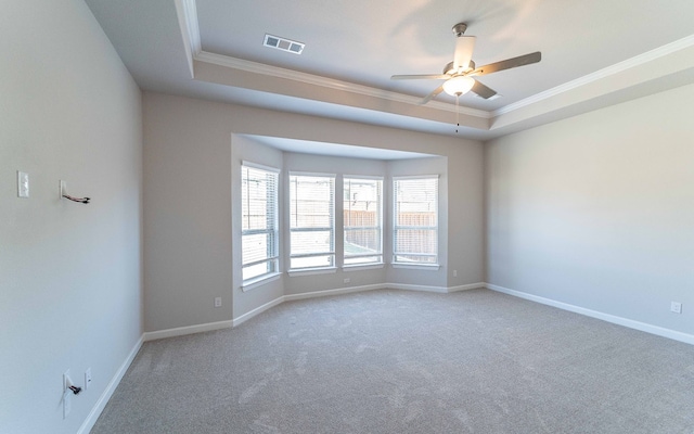 empty room with ceiling fan, a tray ceiling, carpet floors, and ornamental molding