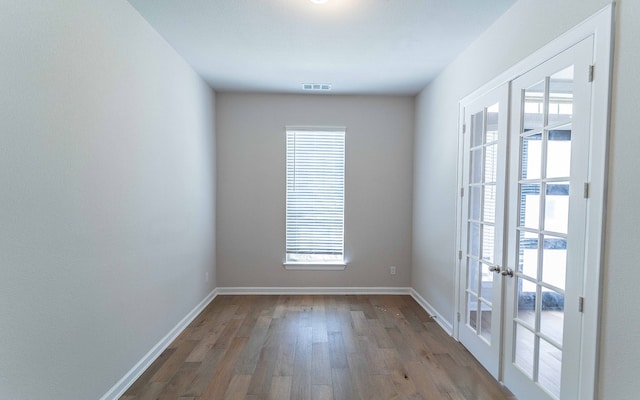 empty room featuring a healthy amount of sunlight, french doors, and wood-type flooring