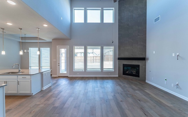 unfurnished living room with a towering ceiling, wood-type flooring, sink, and a tile fireplace