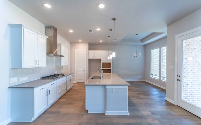 kitchen featuring wall chimney range hood, a center island with sink, dark hardwood / wood-style floors, decorative light fixtures, and sink