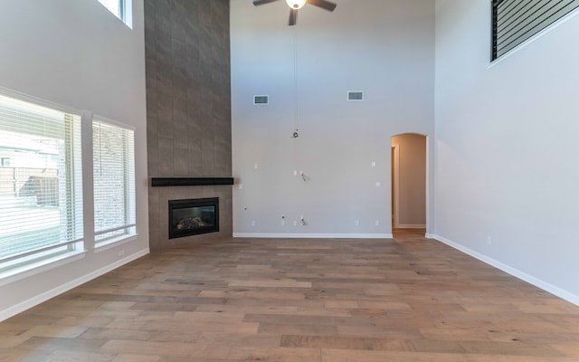 unfurnished living room with a wealth of natural light, a tiled fireplace, wood-type flooring, and ceiling fan