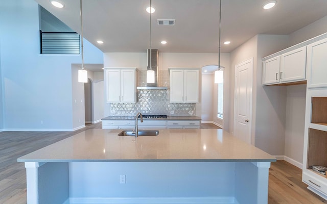 kitchen with wall chimney range hood, hanging light fixtures, a large island, and light wood-type flooring