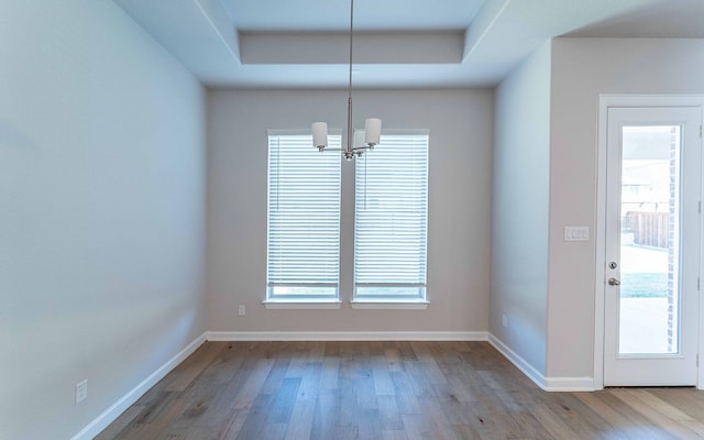 unfurnished dining area with a notable chandelier, a tray ceiling, and hardwood / wood-style flooring