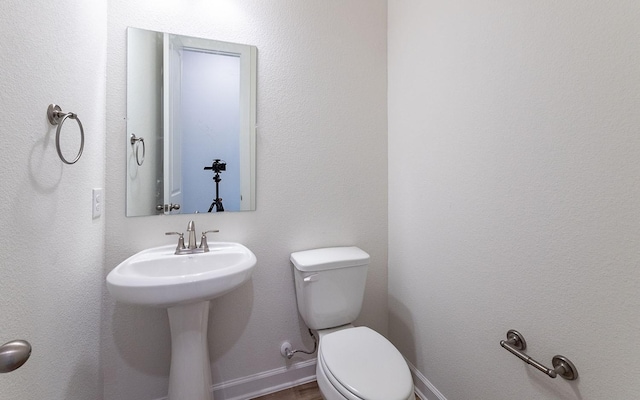 half bath with baseboards, a sink, and toilet