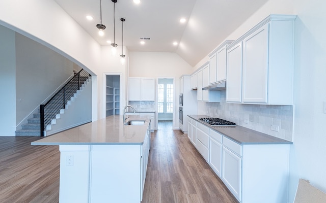 kitchen with light hardwood / wood-style floors, backsplash, a center island with sink, sink, and appliances with stainless steel finishes