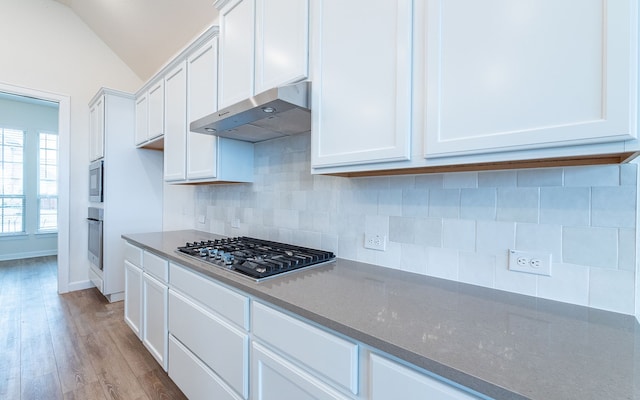 kitchen with light hardwood / wood-style floors, white cabinetry, lofted ceiling, appliances with stainless steel finishes, and tasteful backsplash