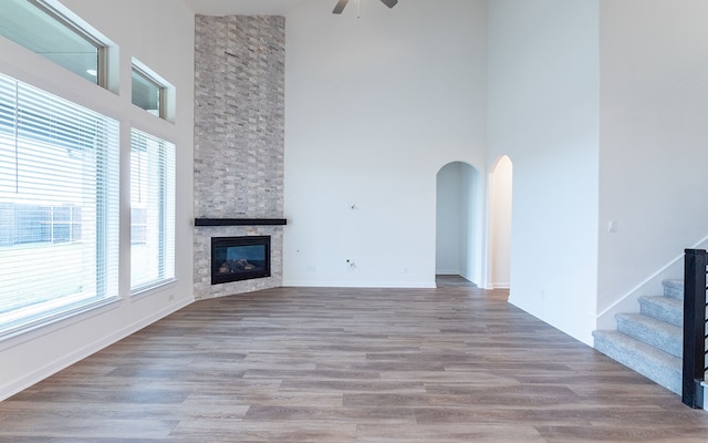 unfurnished living room featuring a stone fireplace, ceiling fan, hardwood / wood-style floors, and a wealth of natural light