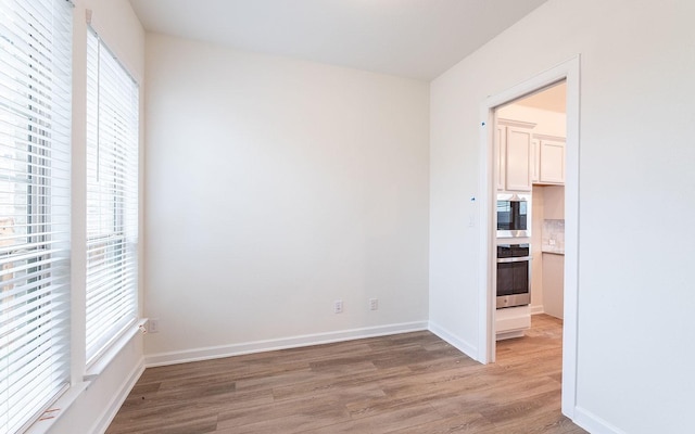 unfurnished room with light wood-type flooring and baseboards