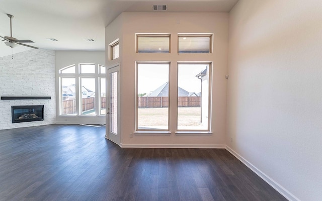 unfurnished living room with dark wood finished floors, visible vents, a stone fireplace, and baseboards