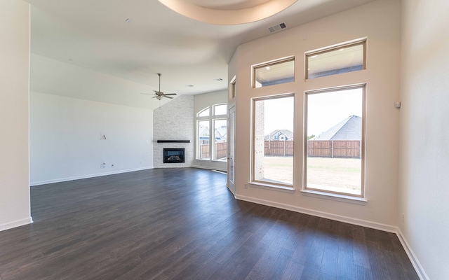 unfurnished living room featuring brick wall, ceiling fan, a fireplace, and dark hardwood / wood-style floors