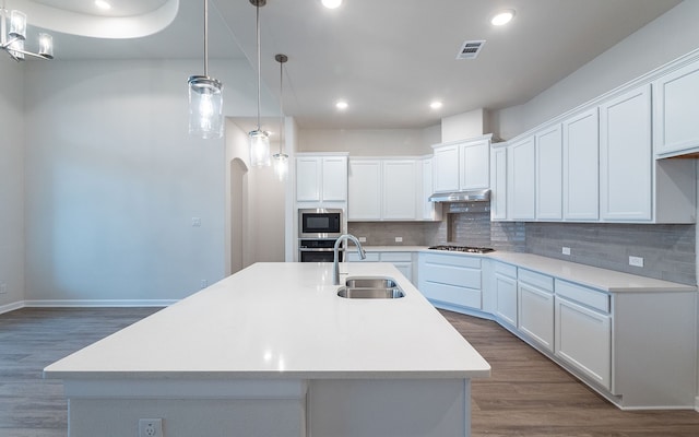 kitchen featuring an island with sink, stainless steel appliances, tasteful backsplash, and wood-type flooring