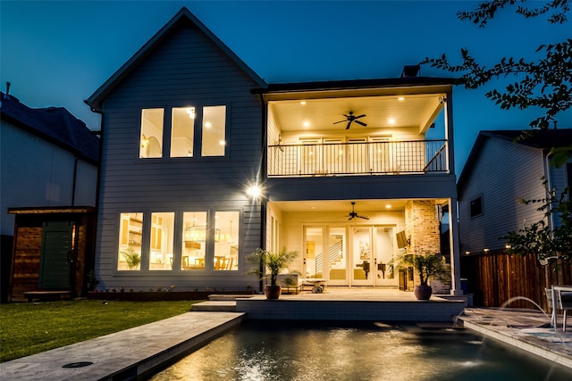 back house at twilight featuring ceiling fan, a balcony, a patio, and a pool