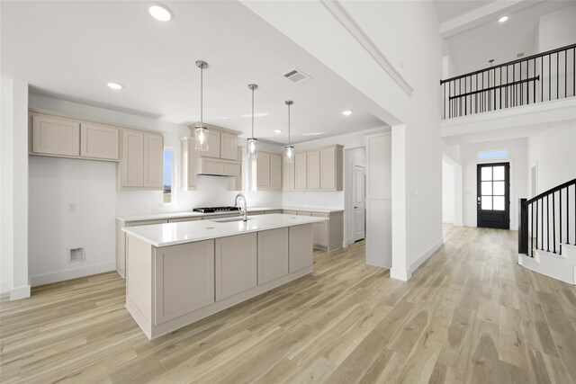 kitchen featuring gray cabinets, light hardwood / wood-style flooring, decorative light fixtures, a kitchen island with sink, and sink