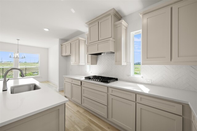 kitchen with light hardwood / wood-style floors, sink, stainless steel gas stovetop, a notable chandelier, and backsplash