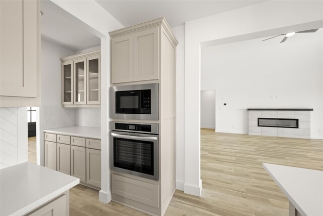 kitchen featuring tasteful backsplash, light hardwood / wood-style flooring, oven, built in microwave, and a fireplace